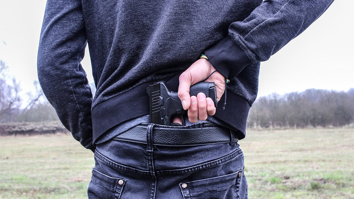 Man carrying a black handgun behind the back