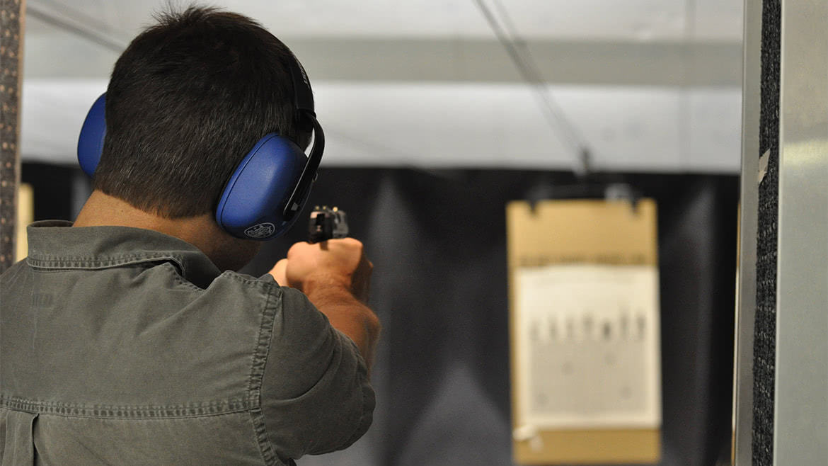 Man shooting in a target using a black pistol at range