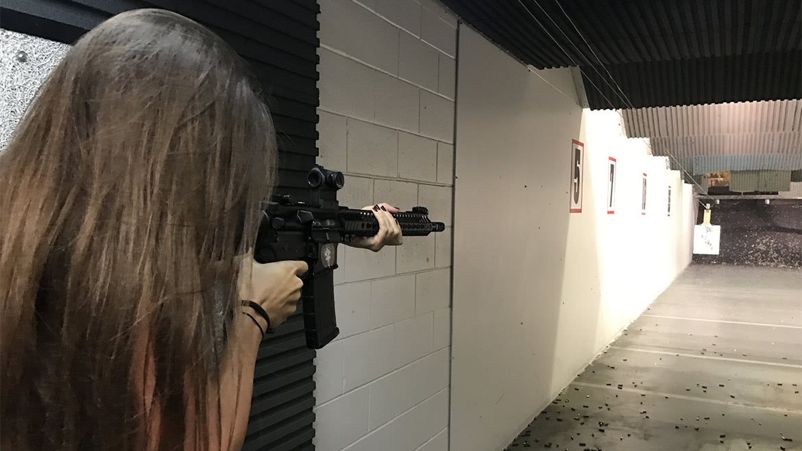 A girl with long hair is holding an assault rifle at range